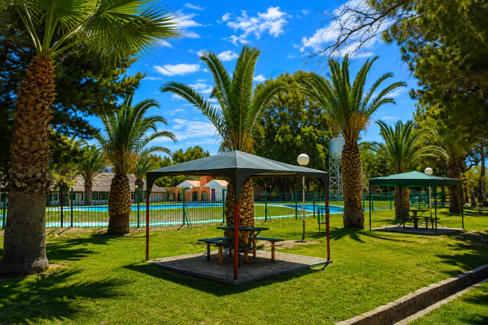Mesas con sombra entre palmeras junto a las piletas